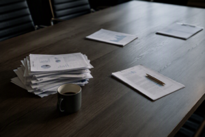 Boardroom table after a meeting, one thick pile of papers heavily worked and two thin piles barely touched beside a cold coffee.