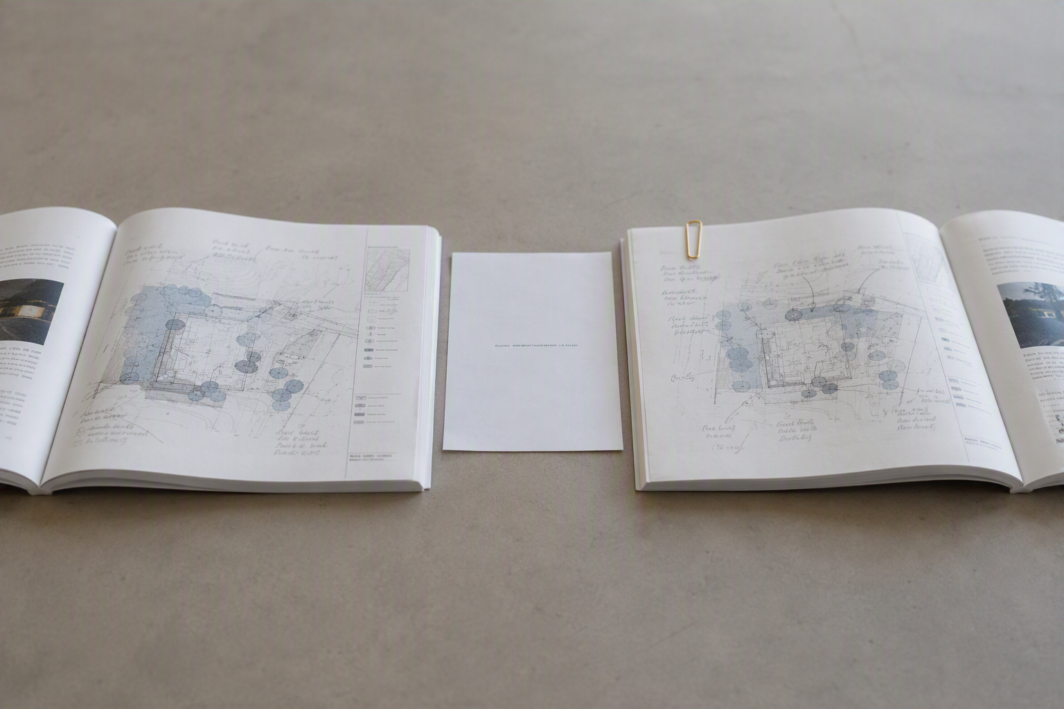 Two identical plan documents open side by side on a desk at visibly different pages, each annotated by a different hand in pencil.